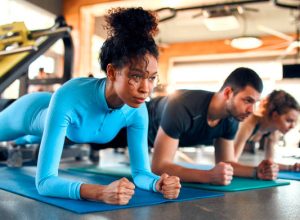 Slim women african american and caucasian ethnicity and muscular man in sportswear doing plank exercise on rubber mat in gym club. The concept of sports and recreation.